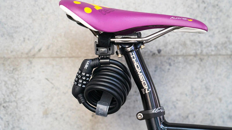 A pink bicycle seat with a black lock attached on a light gray background