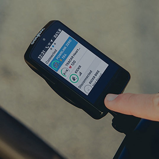 Person holding a WahooCycling Computer with a screen displaying connectivity information against a blurred background