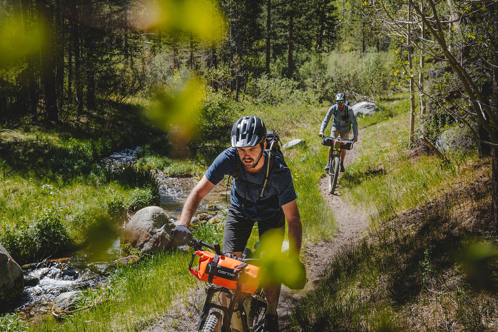 A picture of two guys riding trails on mountain bikes with the Aeroe Spider Handlebar Cradles attached to their bikes with bags