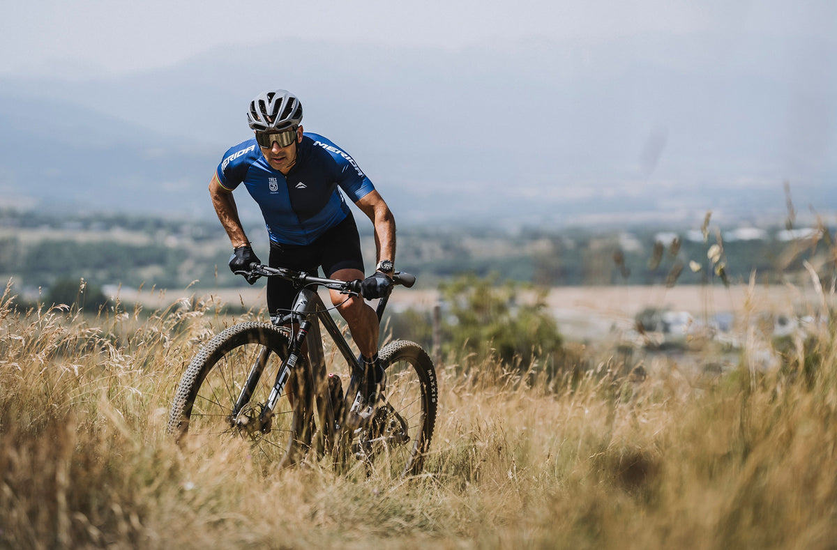 Cyclist riding a mountain bike through a grassy field with a scenic background