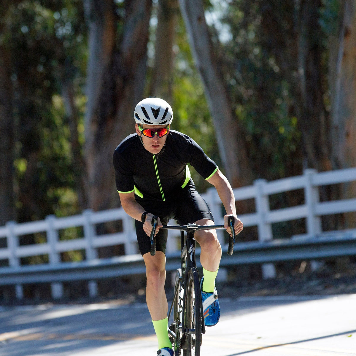 A cyclist riding a road bike wearing black cycling clothing with trees in the background