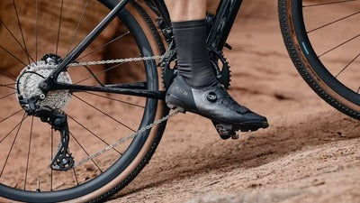 A leg and shoe clipped into mountain bike pedals riding in the dirt