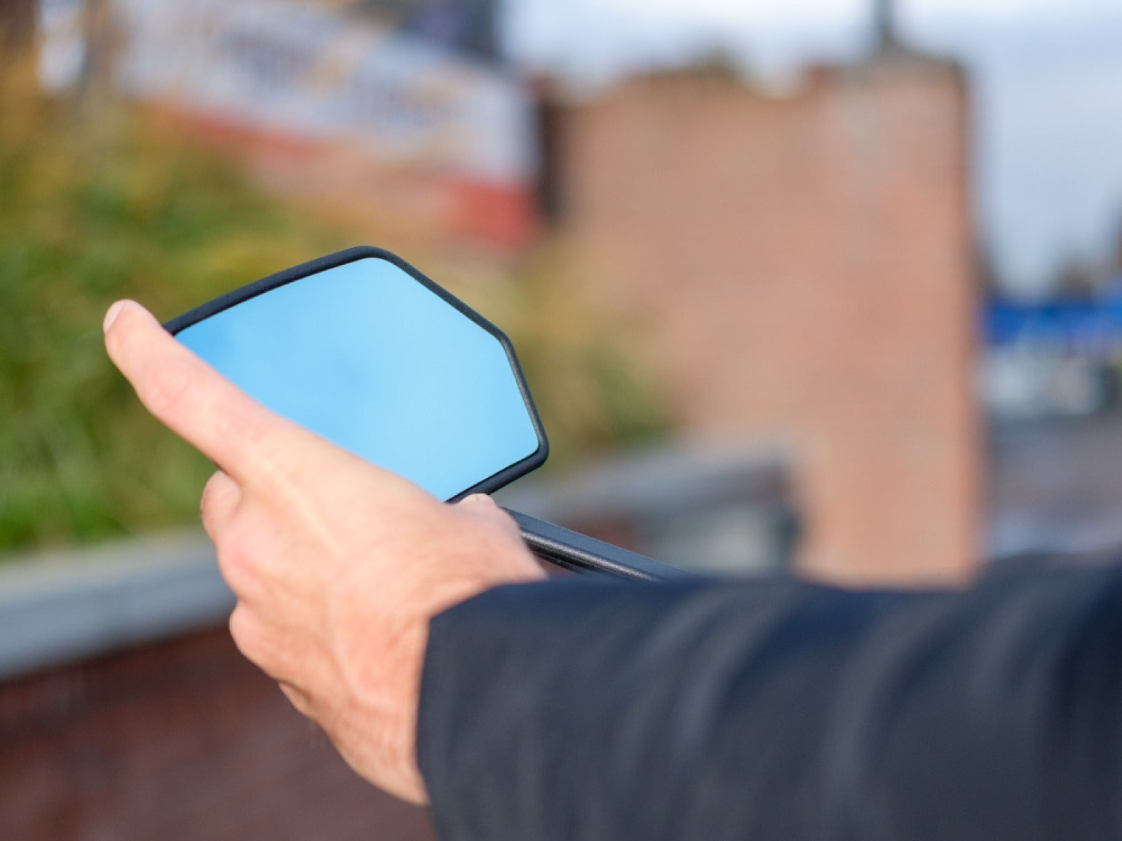 Hand adjusting a bicycle mirror with a blurred outdoor background
