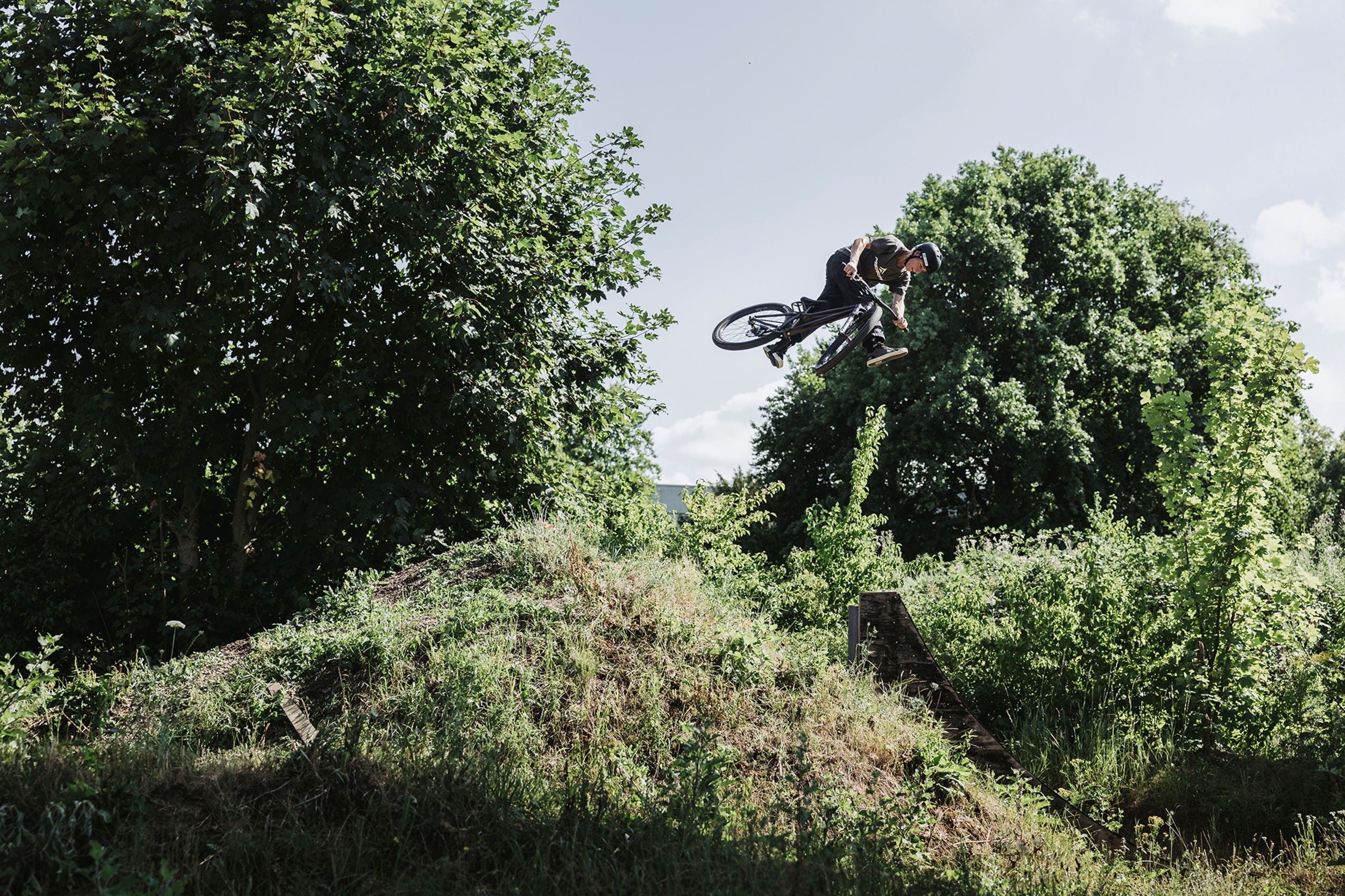 Person on a bicycle performing a jump in a natural setting with trees and grass.