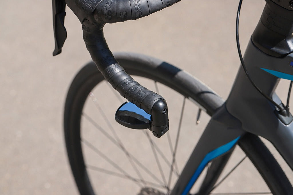 Close-up of a road bike handlebar with a mirror folded away on the drop bar againstaa blurred background