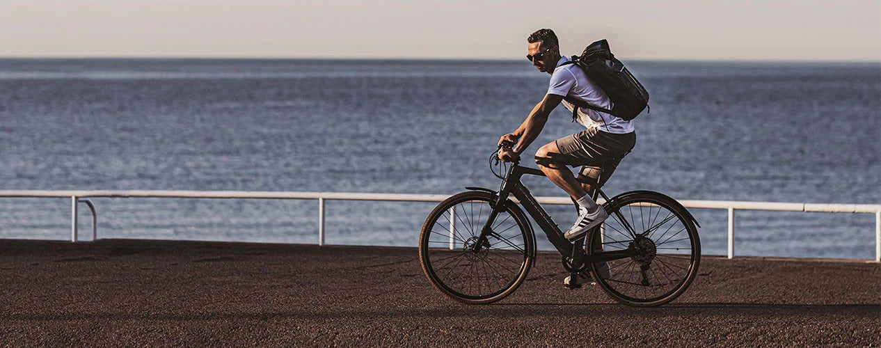Man riding a bicycle along a coastal path with a backpack