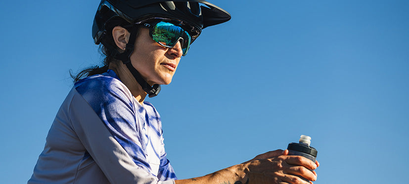 Person wearing a helmet and sunglasses, holding a water bottle against a clear blue sky.
