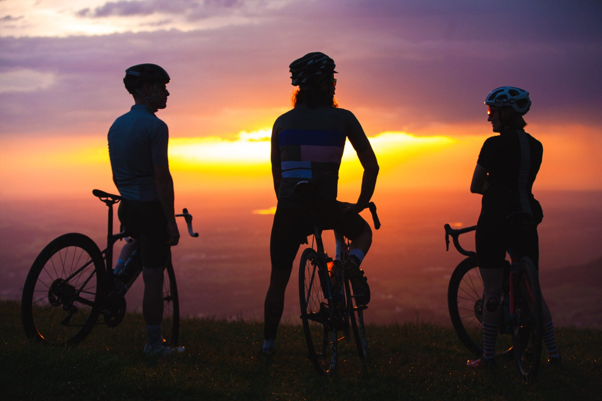 Three cyclists standing with their bicycles against a sunset sky.