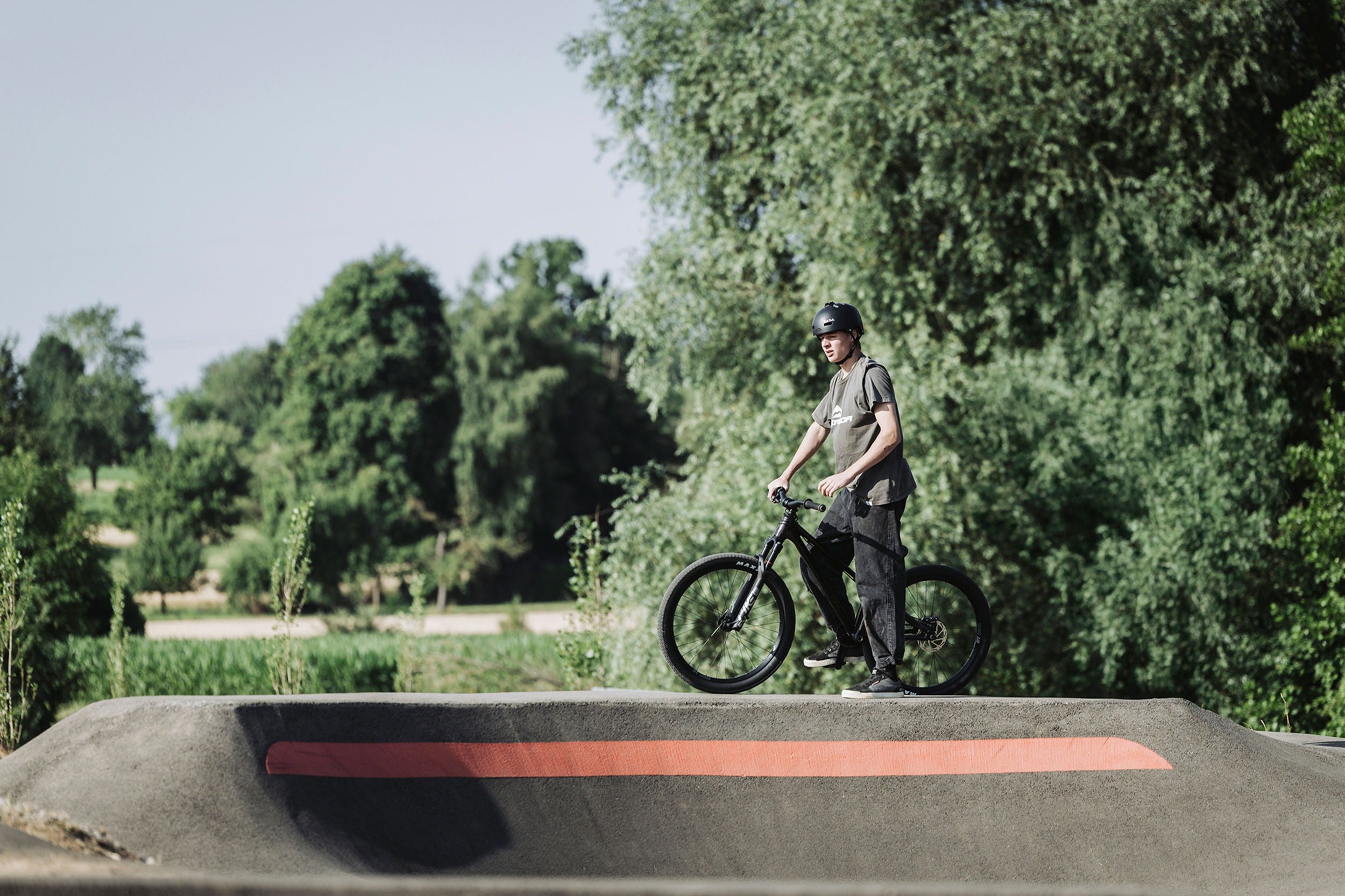 Person with a bicycle on a concrete ramp with greenery in the background