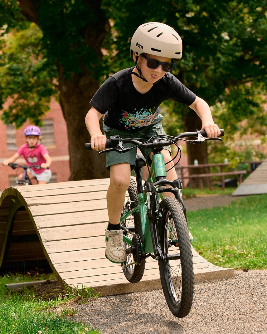 A kid riding a green mountain bike over a an obstacle with an outdoor nature background