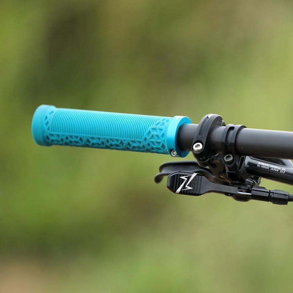 A close-up shot of a bright turquoise blue textured bicycle handlebar grip with a black handlebar and brake lever, set against a blurred green outdoor background.
