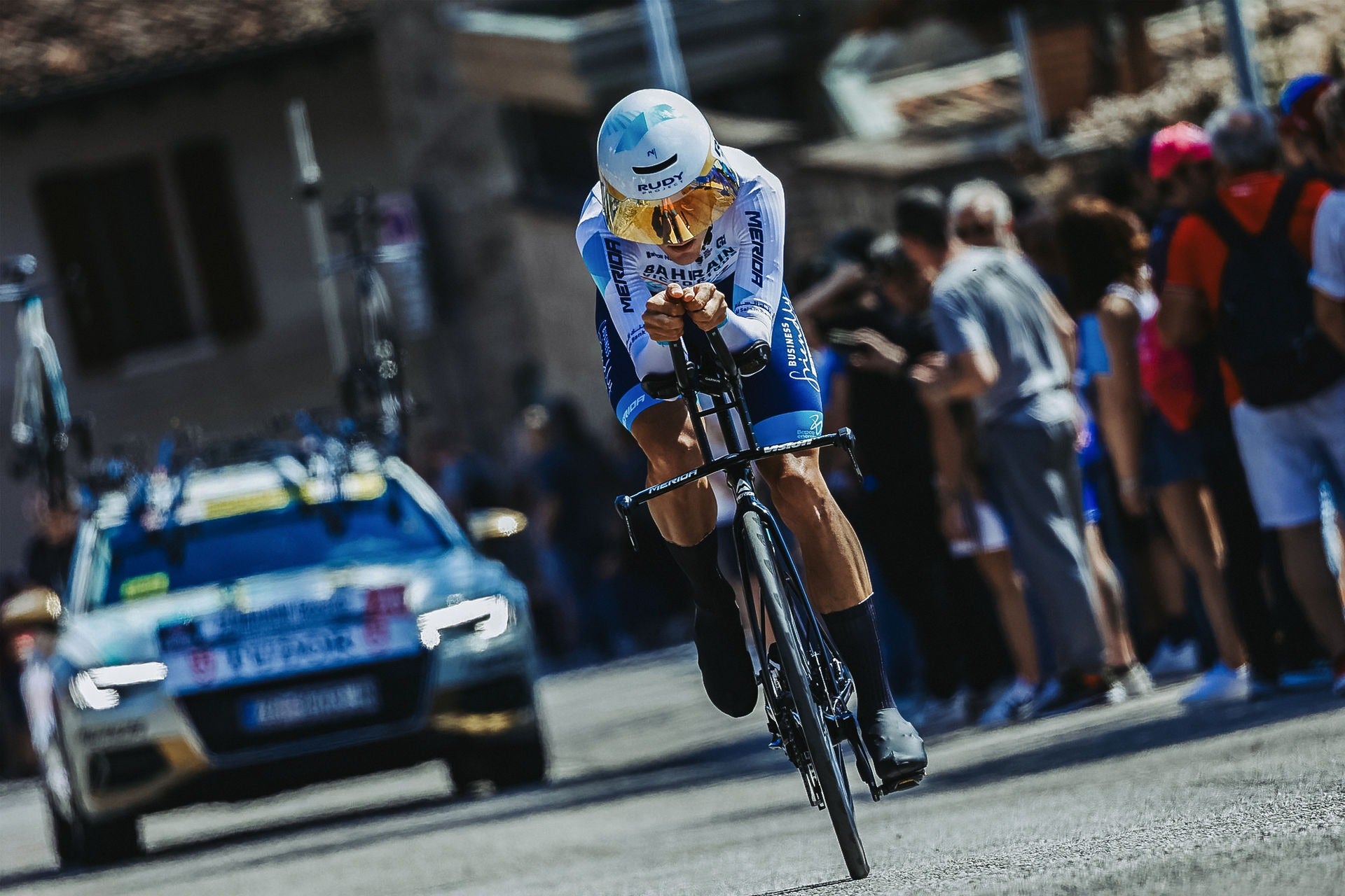 Cyclist on a Tri Bike in a race with a car and spectators in the background