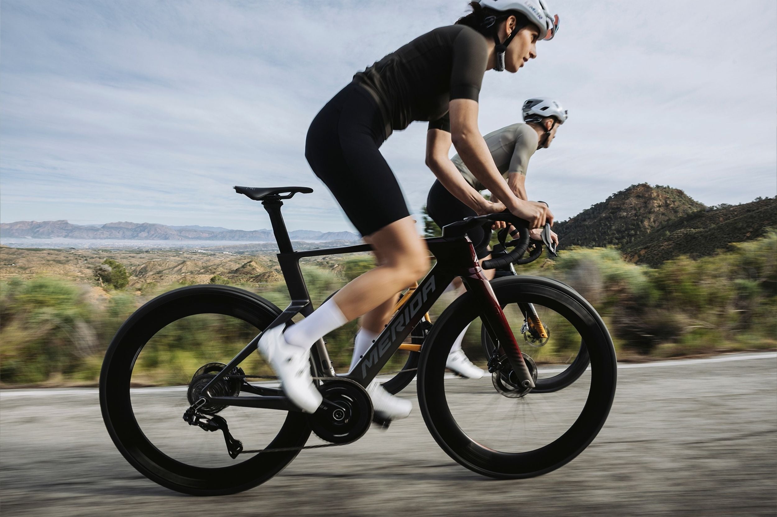Two cyclists riding on a road with a scenic background