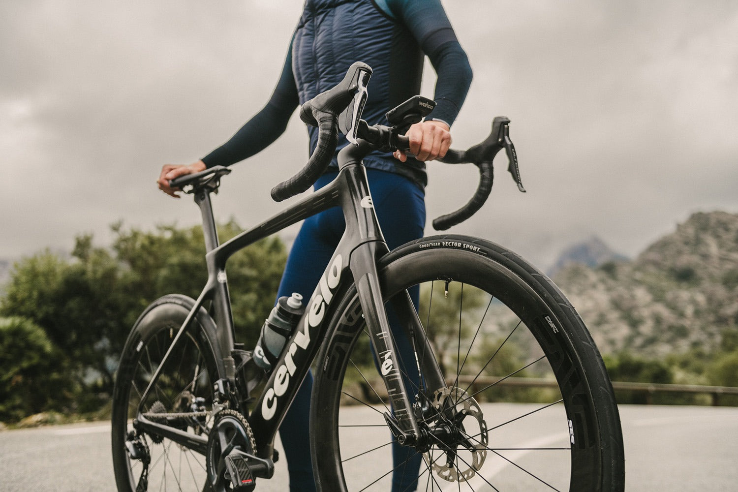 Person holding a Cervelo bicycle on a road with mountains in the background