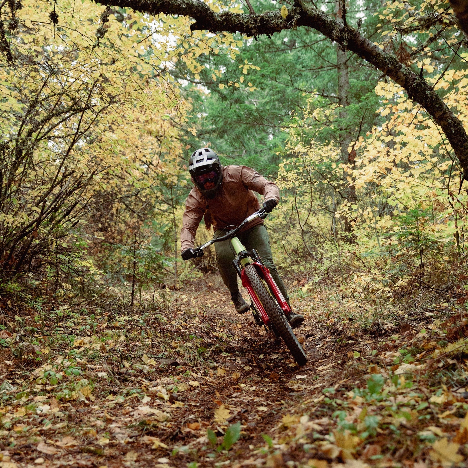 Person riding a mountain bike wearing a full face mountain bike helmet through a forest during autumn.