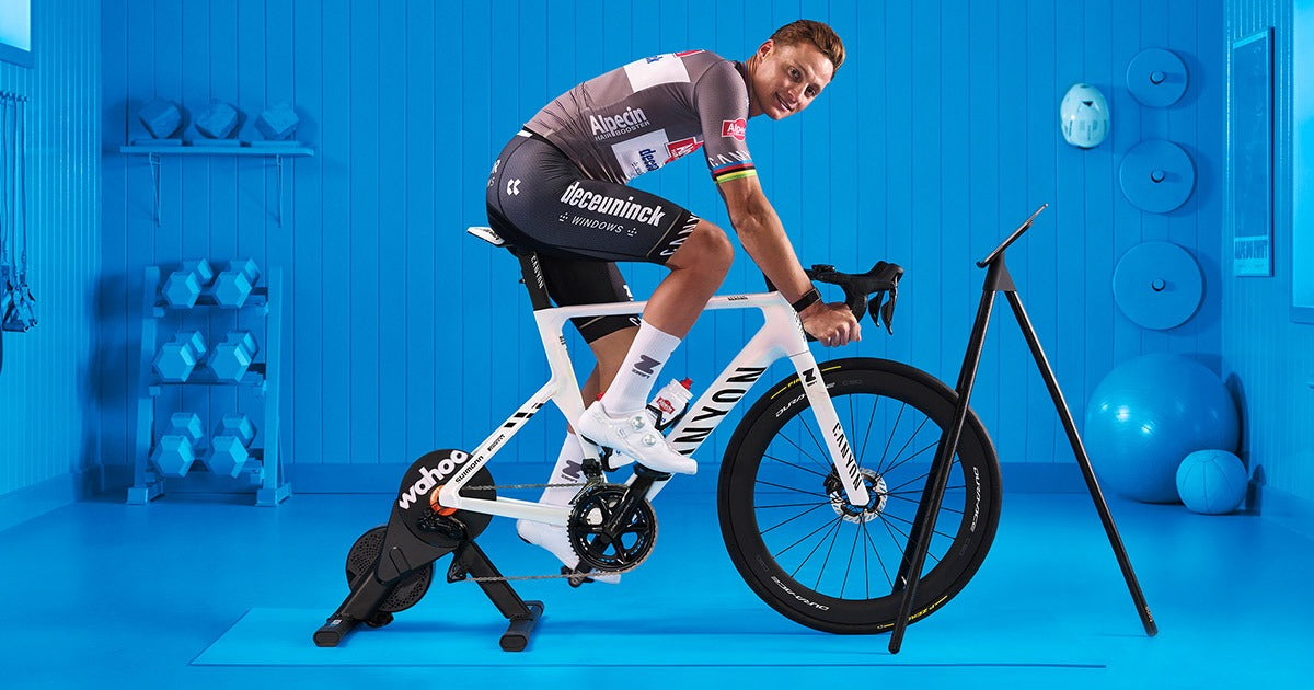 Person on a stationary bike on a Wahoo Indoor Trainer in a blue room with exercise equipment.