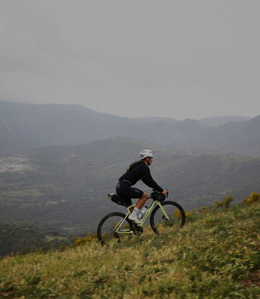 Person riding a gravel bike on a hill with a scenic view of mountains in the background