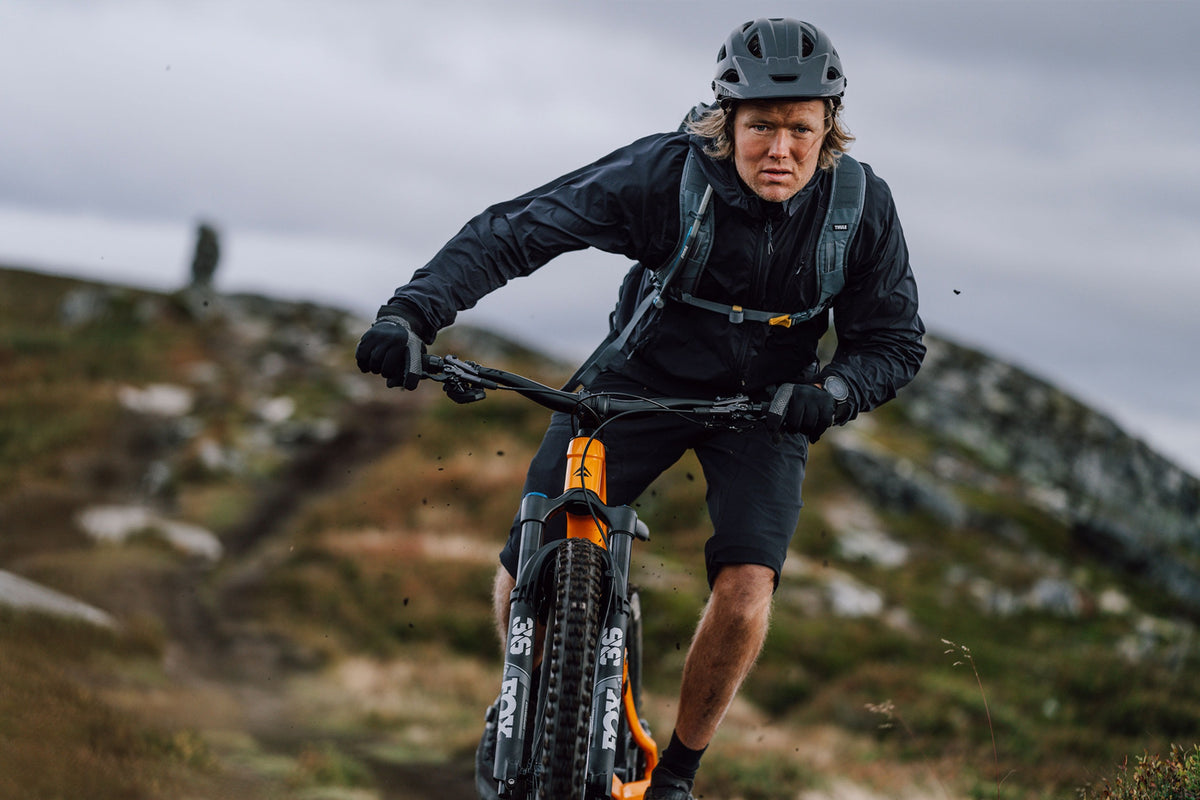 A mountain biker riding towards the camera on an orange mountain bike with blurred mountains in the background