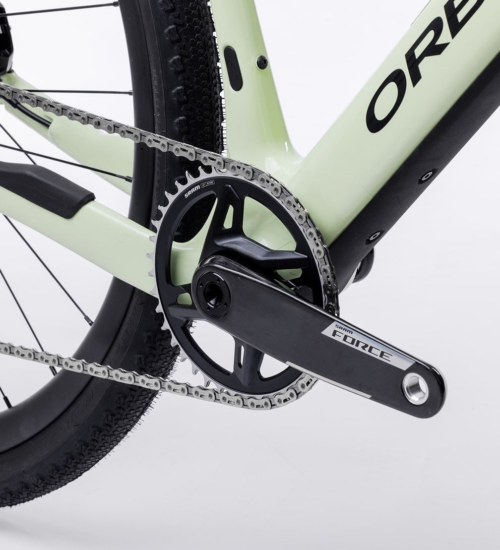 Close-up of an Orbea Gravel Bike front chain and gear system on a light green frame against a white background.