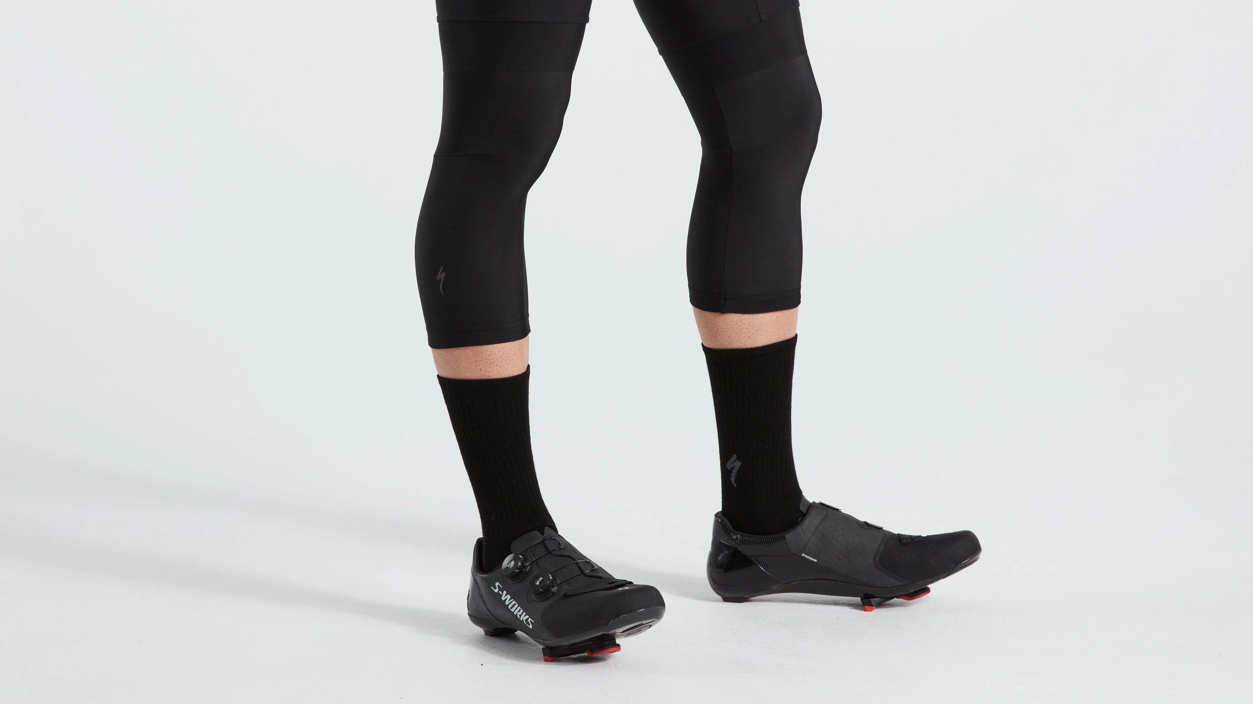 Person wearing black cycling shoes, black cycling shorts with knee warmers on a white background