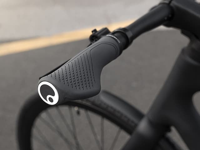 Close-up of a bicycle handlebar with a brand logo on the grip on a blurred road background