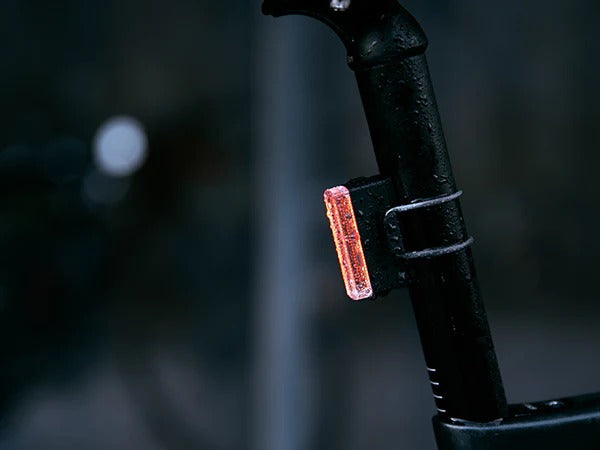Close up of a rear bright red bicycle tail light attached to a bike on a dark, blurred background