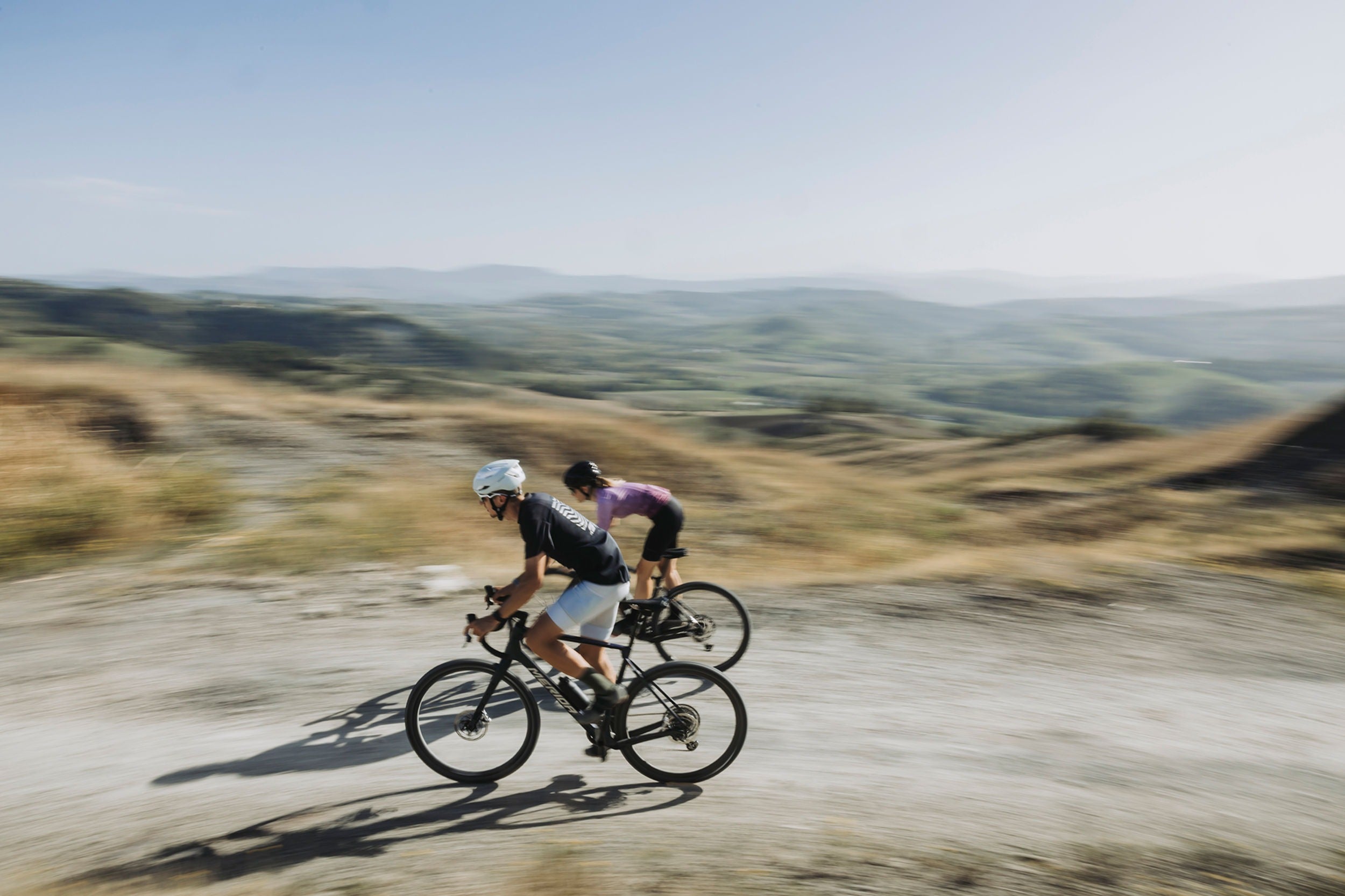 Two Gravel Cyclists riding on a dirt path with a scenic landscape in the background