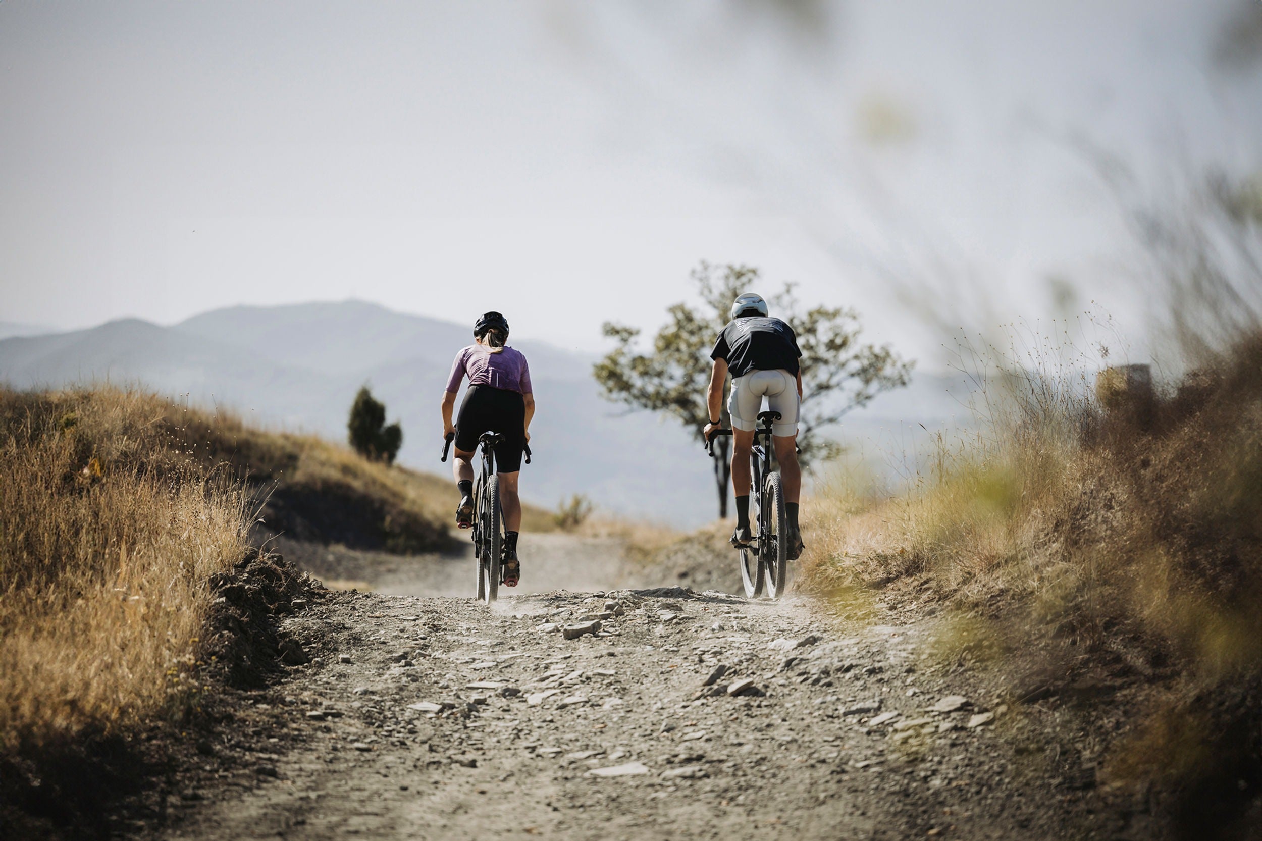 Two gravel cyclists riding on a dirt path with mountains in the background