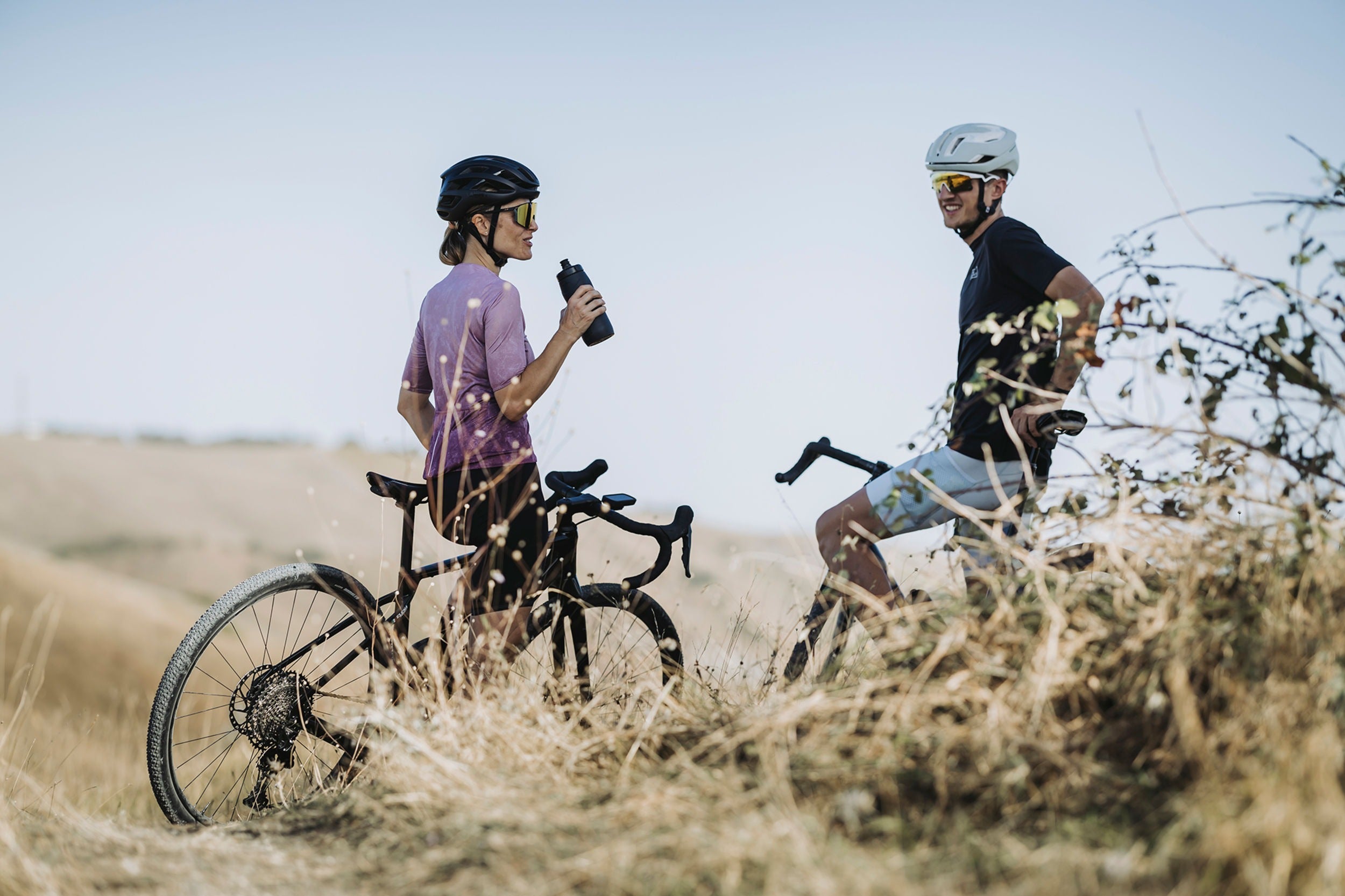 Two gravel cyclists with their bikes in a field on a clear day