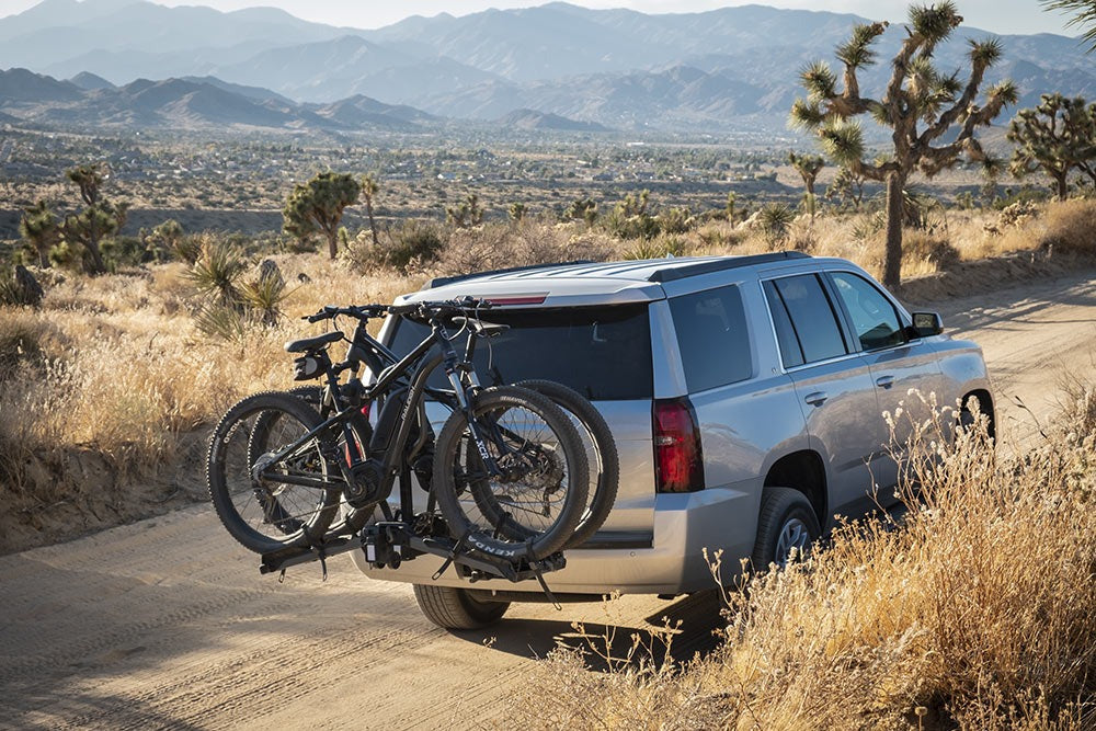 Silver SUV with bicycles on a bike rack in a desert landscape with mountains in the background.