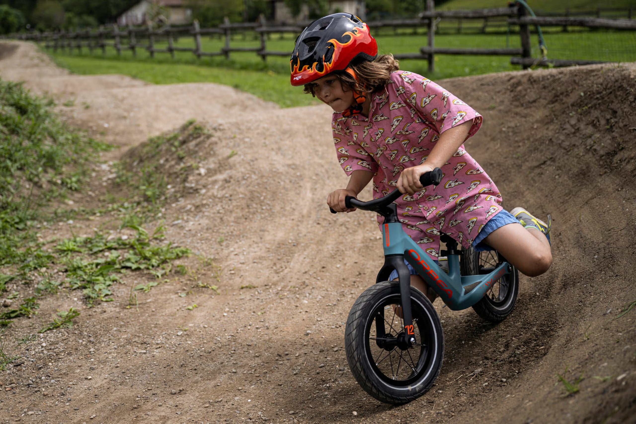 Child riding a balance bike on a dirt path with a helmet