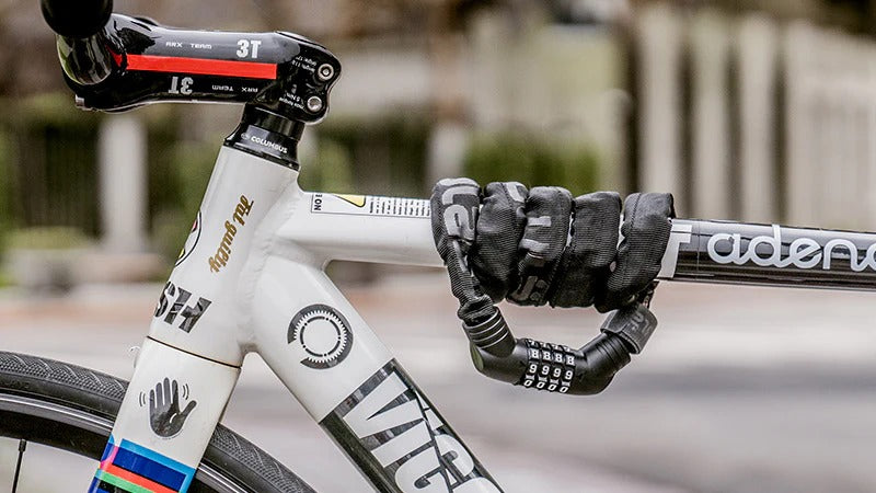 Close-up of a bicycle frame with a lock wrapped around the top tube against a blurred urban setting