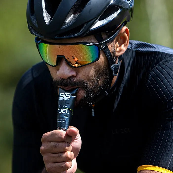 Cyclist wearing a helmet and sunglasses holding a energy gel container.