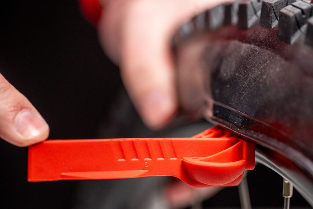 Close-up of a hand using a red tyre lever tool on bicycle tyre on a black background