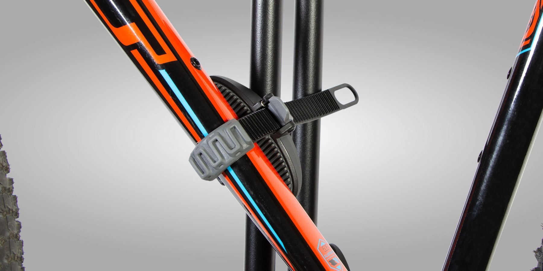 Close-up of a bicycle frame with orange and black design strapped onto a bike rack on a gray background