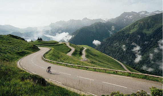 A road biker on a winding mountain road with greenery and mountains in the background