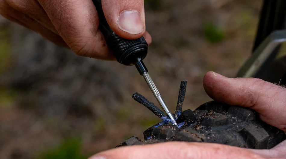Person using a Muc-Off Precision Tubeless Repair Capsule to repair a puncture on a blurred outdoor background