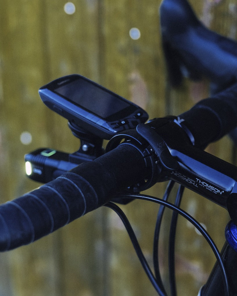 Close-up of road handlebars with a screen, Knog Bell and light against a blurred natural background