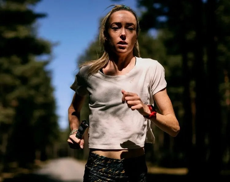 Woman running outdoors holding a SIS energy gel in her hand with a blurred background