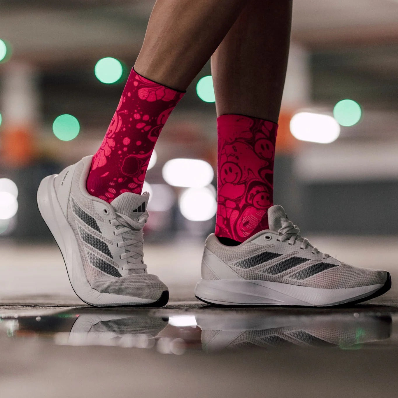 A close up of legs with bright pink socks with smiley face pattern wearing white trainers on a blurred urban background