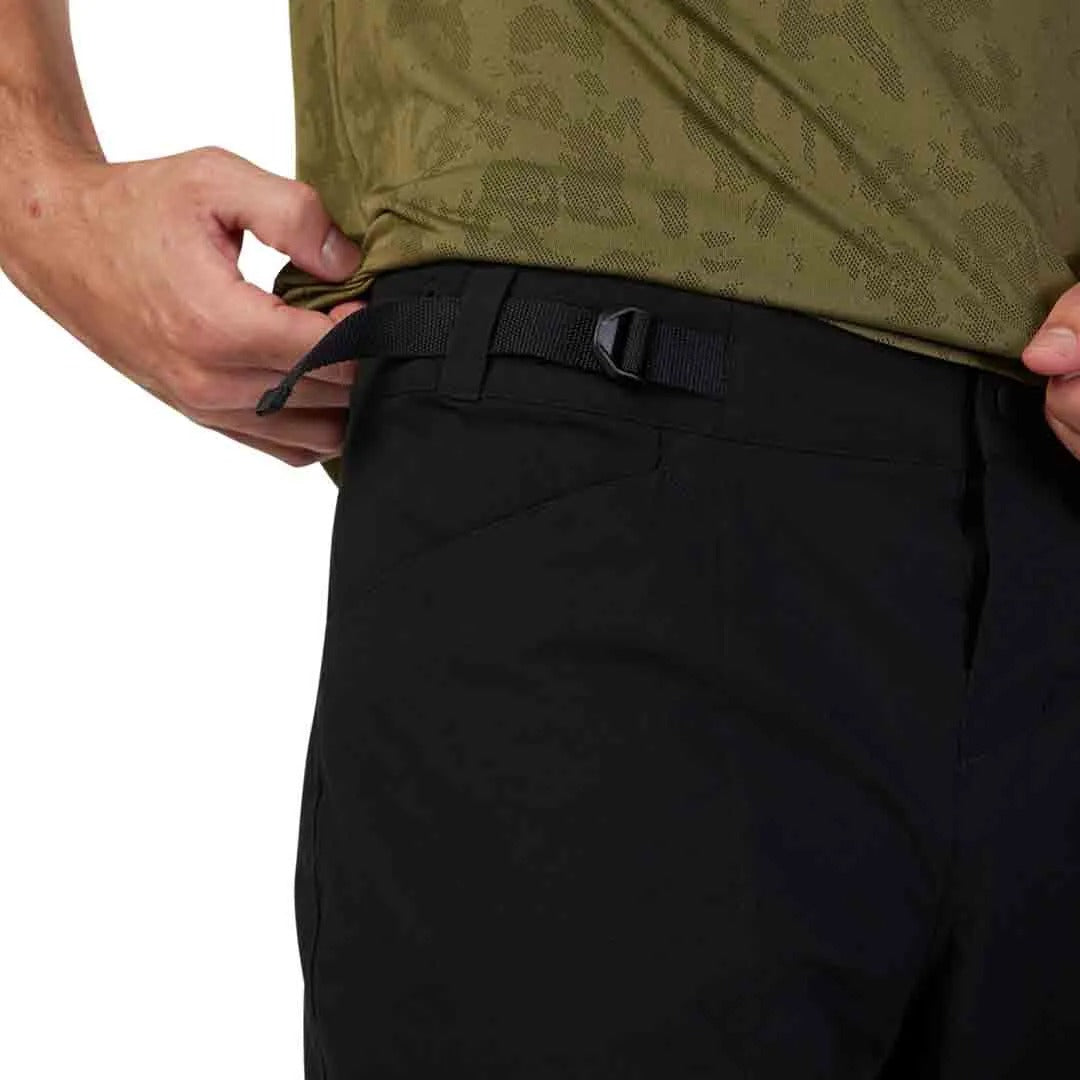 A picture of someone tucking an olive green shirt into a pair of black mountain bike shorts on a white background