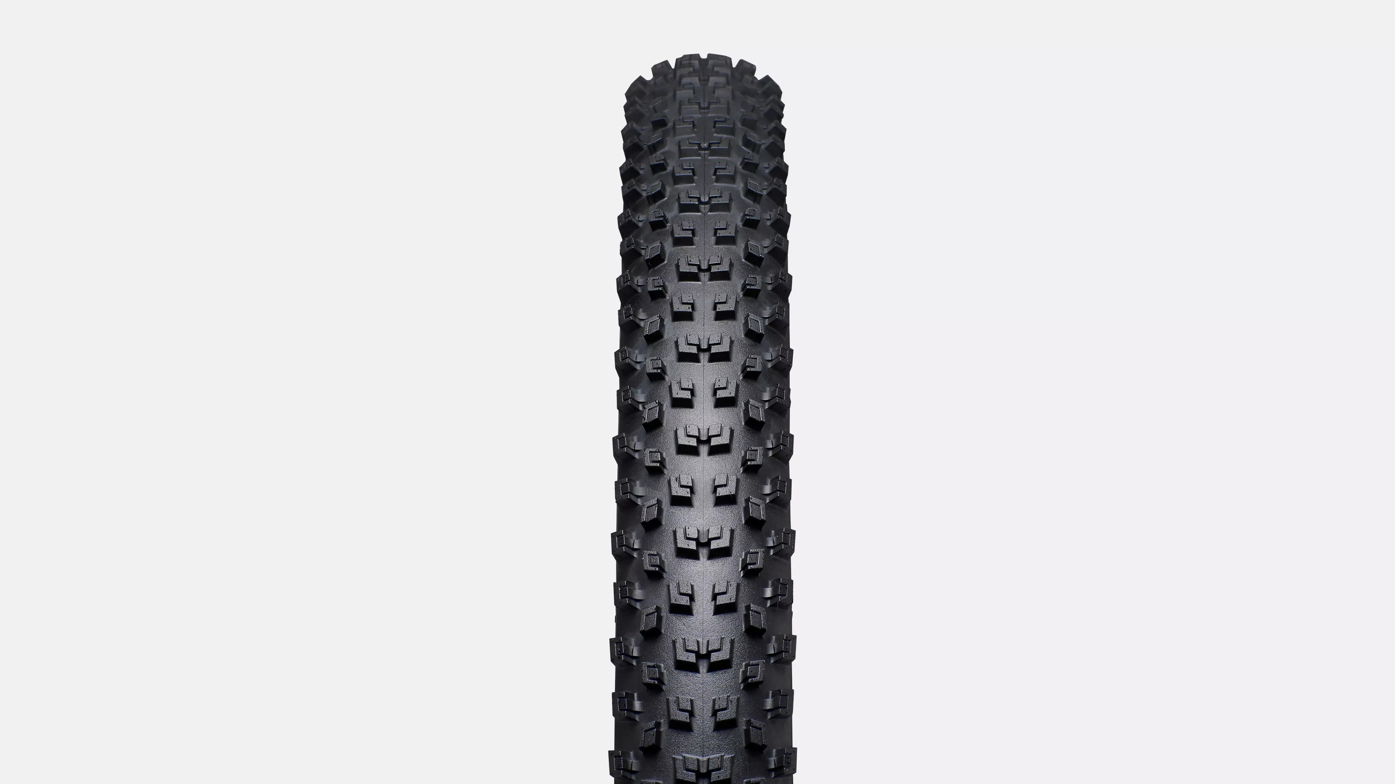 Black off-road tyre with tread pattern on a light gray background