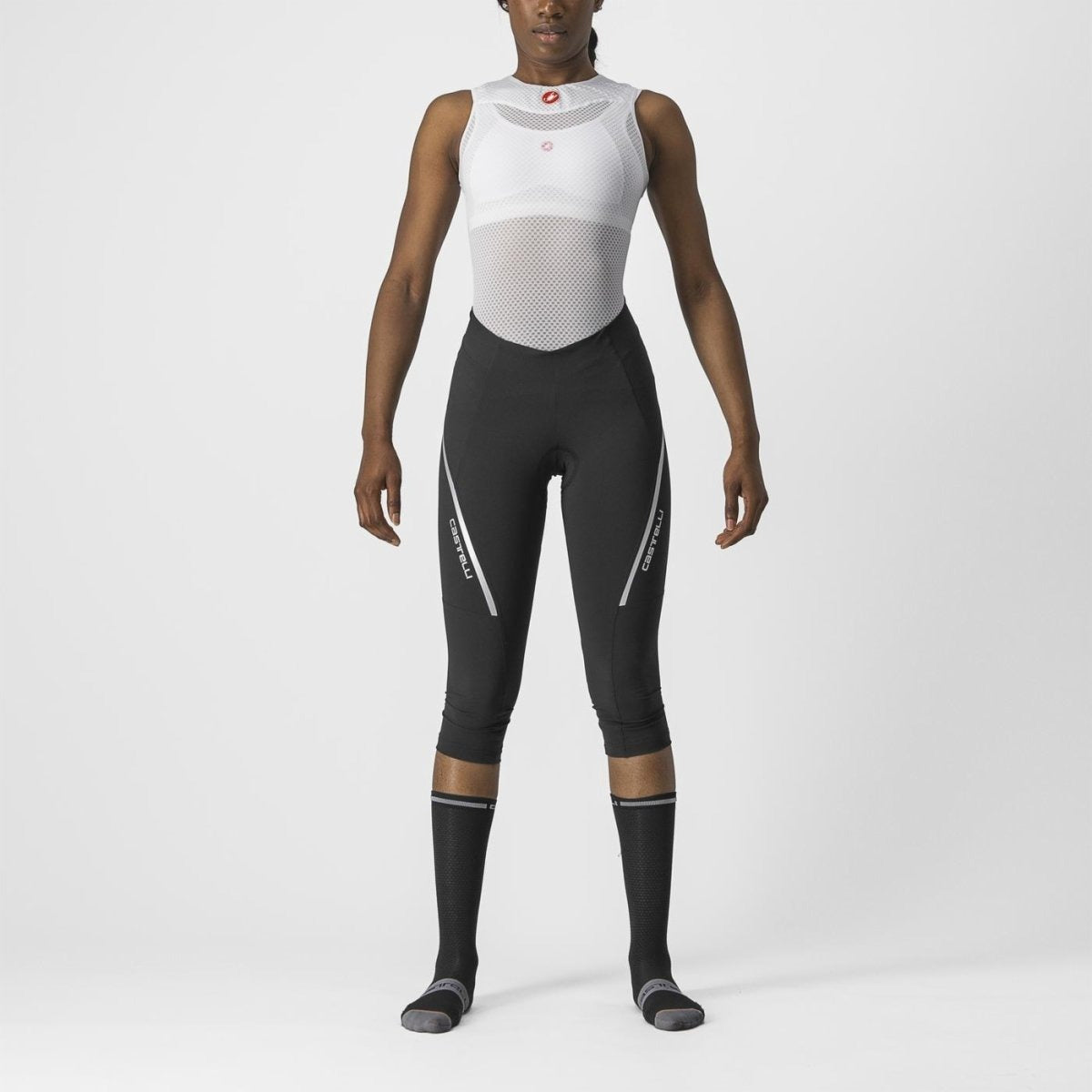 Person wearing a white sleeveless top and black Castelli cycling pants on a white background