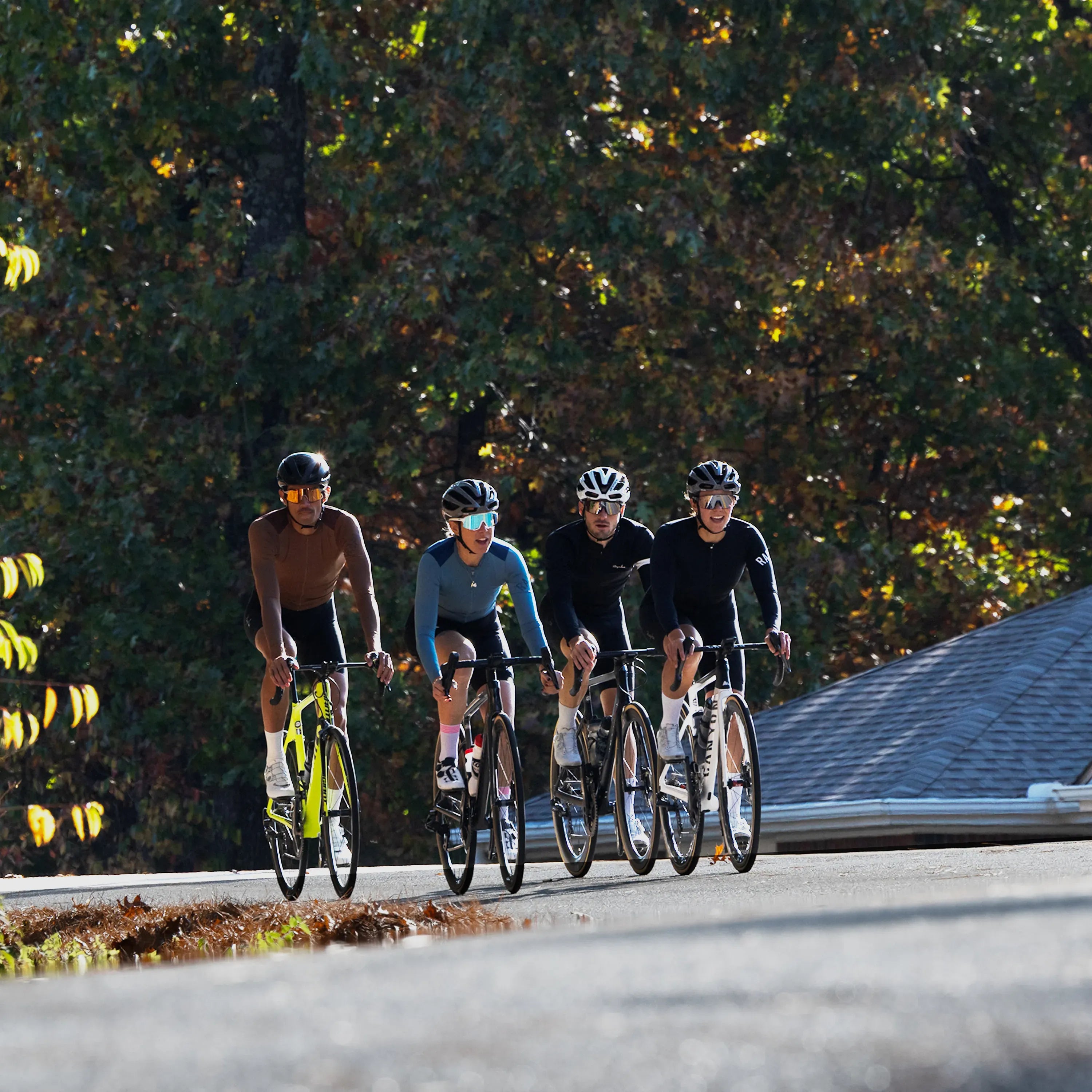 Four cyclists riding together on a road with trees in the background