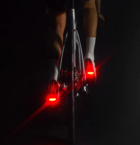 Cyclists pedaling on a road bike in the dark displaying lights on the back of the pedals