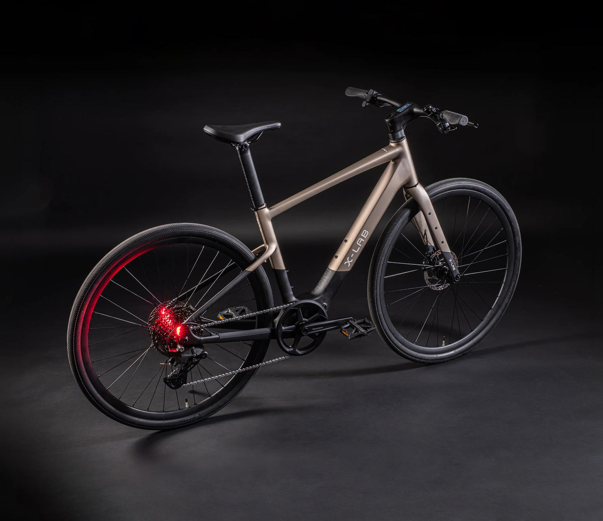 A sleek electric bicycle with a matte taupe frame and black components, shown on a dark studio background with red lighting accents.