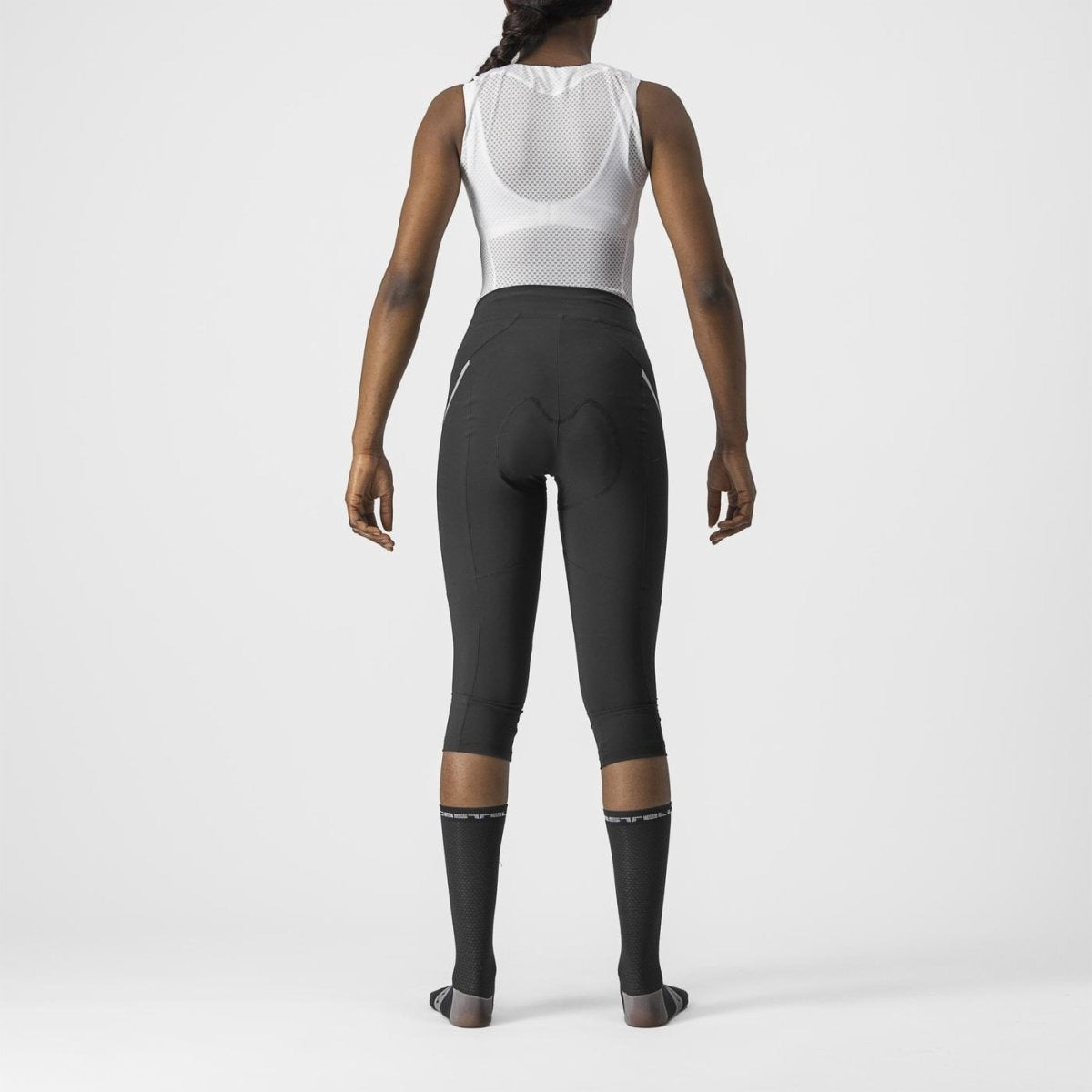 Person wearing a white sleeveless top and black Castelli cycling pants shown from the back on a light gray background