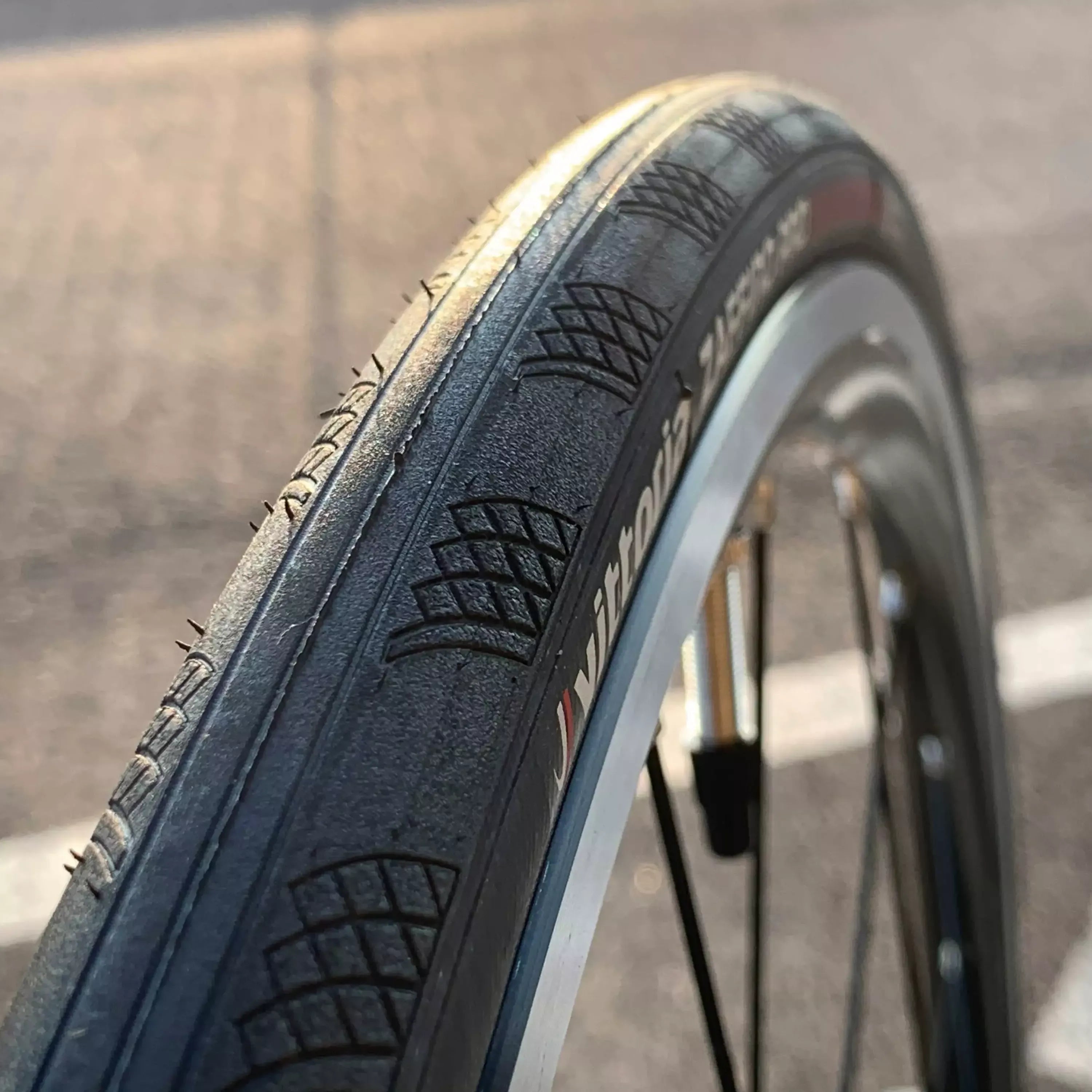 Close-up of a Vittoria bicycle tyre with tread pattern on a blurred road background