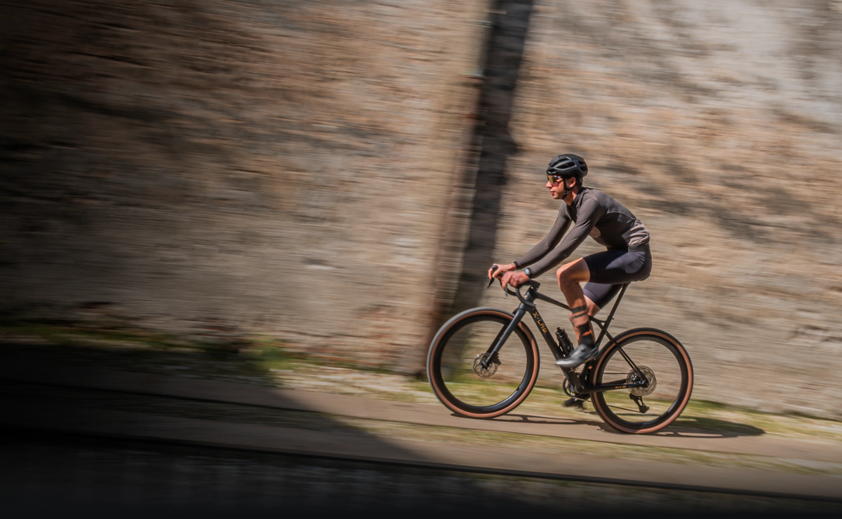 Person cycling on a black X-LAB Gravel Bikeon a path with a blurred background