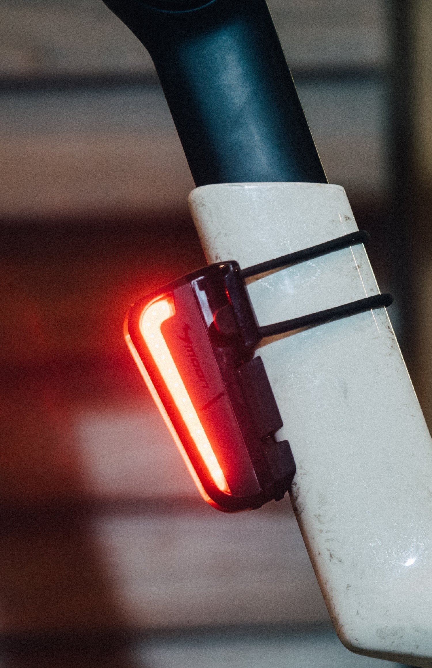 Red bicycle tail light attached to a bike frame with a blurred background